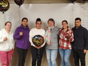 2023-24 English Class. One man and five women standing in front of white board with balloons.